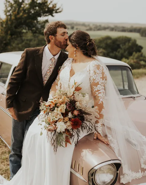 A bride and groom posing with a large, artistic wedding bouquet featuring mixed flowers and greenery.