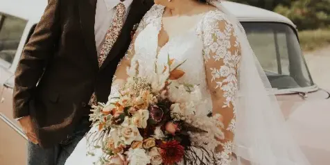 A bride and groom posing with a large, artistic wedding bouquet featuring mixed flowers and greenery.
