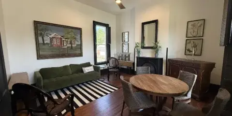 Interior view of The Hoffman House event venue showing a living area with a green sofa and a dining area with a round wooden table.