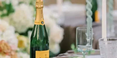 A close-up of an elegant wedding table setting featuring a bottle of Veuve Clicquot champagne, white floral arrangements, and crystal glassware.