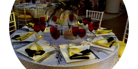 A formal event table setting featuring a floral centerpiece, red wine glasses, and yellow napkins.