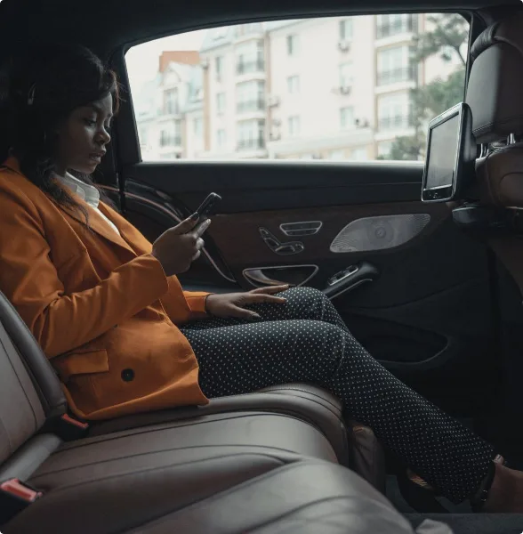 Passenger seated in the back of a luxury sedan with leather interior and rear-seat screen