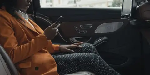 Passenger seated in the back of a luxury sedan with leather interior and rear-seat screen