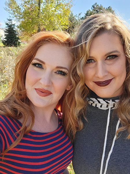 Two women with styled hair and professional makeup posing outdoors.