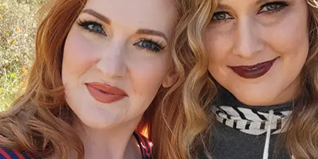 Two women with styled hair and professional makeup posing outdoors.