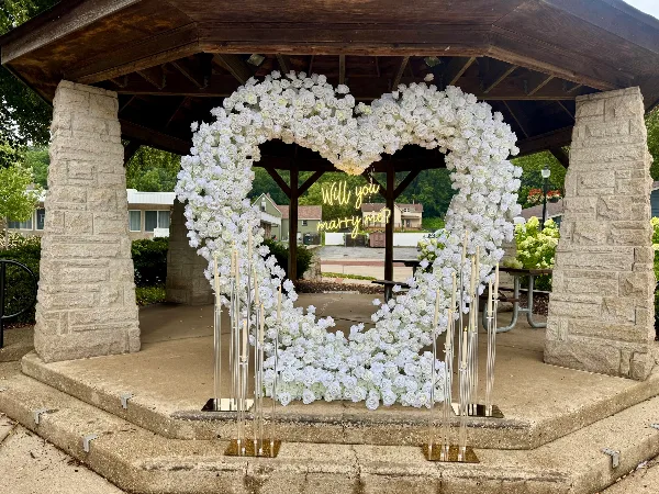 A large white floral heart arch with tall candles set up in a stone gazebo.