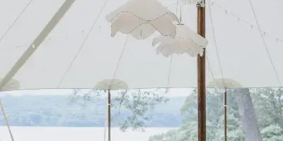 Elegant wedding reception tables with floral centerpieces and hanging lights inside a large white tent.