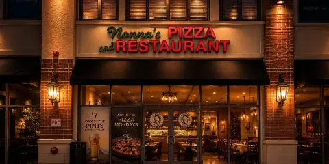 Exterior view of Nonna's Pizza and Restaurant storefront at night, showing the illuminated sign and dining room through the windows.