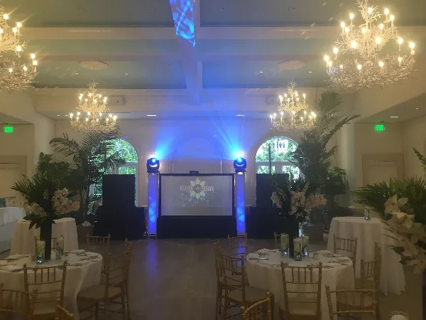 Wedding reception hall with a DJ booth, blue stage lighting, and a projection screen.