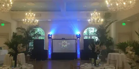 Wedding reception hall with a DJ booth, blue stage lighting, and a projection screen.