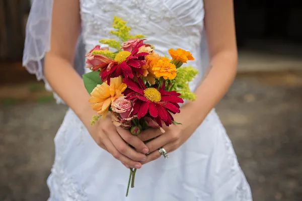 A bride in a white dress holding a colorful bouquet of red, orange, and yellow flowers.