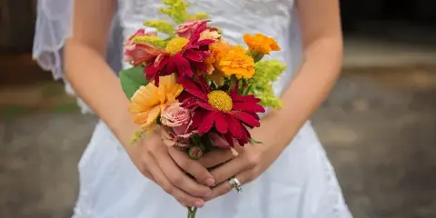 A bride in a white dress holding a colorful bouquet of red, orange, and yellow flowers.
