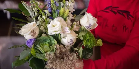 A person in a red 'Talk ta Me' shirt holding a custom bouquet of white roses with personalized messages embossed on the petals.