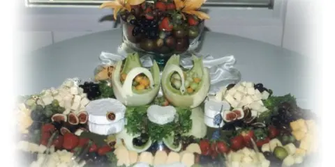 A catering display featuring a cheese and fruit platter with decorative garnishes.