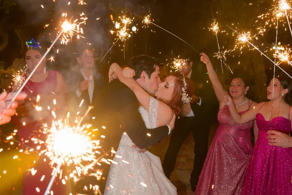 A bride and groom kiss during a sparkler exit at a wedding reception, surrounded by guests holding sparklers.