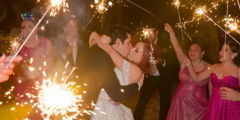A bride and groom kiss during a sparkler exit at a wedding reception, surrounded by guests holding sparklers.