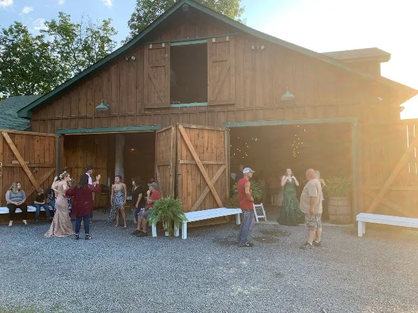 A rustic wooden barn venue with open doors and guests standing on a gravel patio.