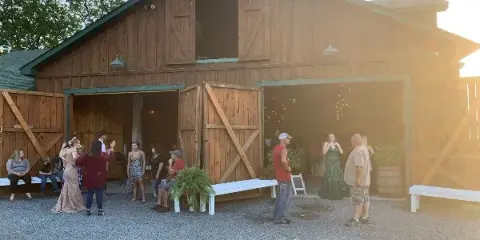 A rustic wooden barn venue with open doors and guests standing on a gravel patio.
