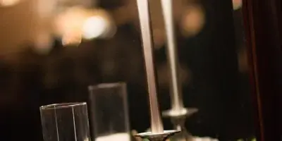 A close-up of an elegantly styled event table featuring a tall lamp, pillar candles in glass holders, a geometric terrarium, and a pink peony flower.