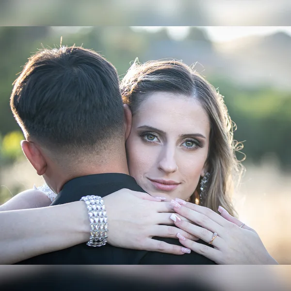 A professional wedding photograph showing a bride and groom embracing, with the bride looking at the camera.