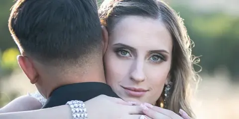 A professional wedding photograph showing a bride and groom embracing, with the bride looking at the camera.