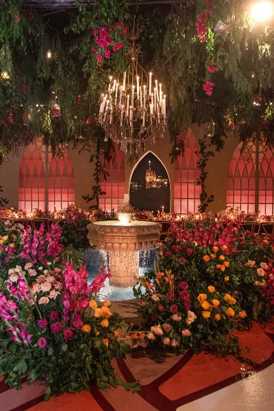 An indoor event venue featuring a central fountain, a large chandelier, and elaborate floral arrangements in pink and orange tones.