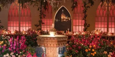 An indoor event venue featuring a central fountain, a large chandelier, and elaborate floral arrangements in pink and orange tones.