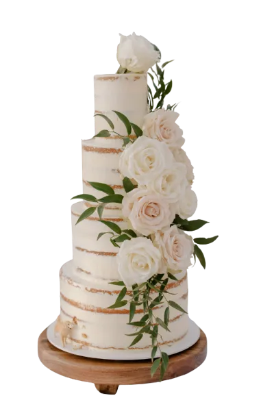 A four-tier semi-naked wedding cake decorated with white roses and eucalyptus leaves on a wooden stand.