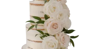 A four-tier semi-naked wedding cake decorated with white roses and eucalyptus leaves on a wooden stand.