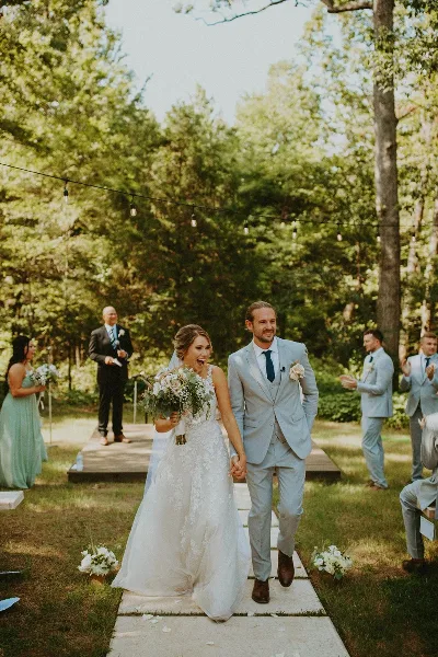 A bride and groom walking down an outdoor aisle with wedding party members in the background.