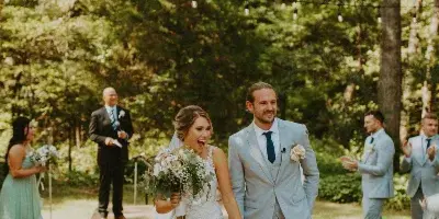 A bride and groom walking down an outdoor aisle with wedding party members in the background.