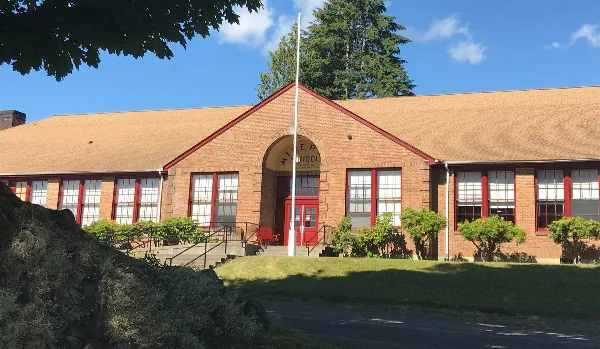 Exterior view of the Mineral Schoolhouse, a historic brick building with a red door and arched entrance, set against a blue sky.