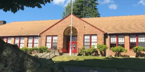Exterior view of the Mineral Schoolhouse, a historic brick building with a red door and arched entrance, set against a blue sky.