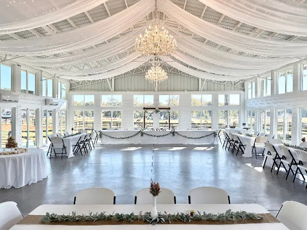 Interior of a white wedding reception hall with a dance floor, chandeliers, and a decorated head table.