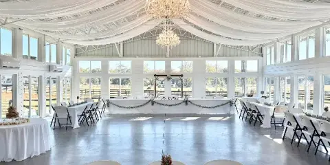 Interior of a white wedding reception hall with a dance floor, chandeliers, and a decorated head table.