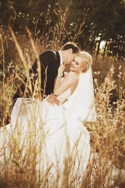 A bride and groom sharing a kiss in a field of tall grass during golden hour.