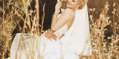 A bride and groom sharing a kiss in a field of tall grass during golden hour.