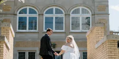 A bride and groom holding hands on the stone steps of a large brick building.