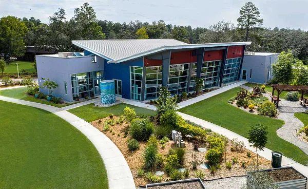 Aerial view of the WellCome OM Center building featuring a modern design with blue and red accents, surrounded by landscaped gardens and a paved walkway.