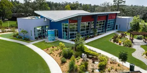 Aerial view of the WellCome OM Center building featuring a modern design with blue and red accents, surrounded by landscaped gardens and a paved walkway.