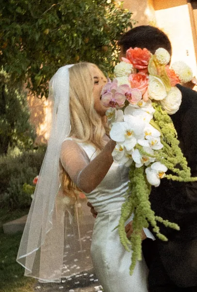 A bride in a white dress and veil holds a large, cascading bouquet of white orchids and greenery while embracing a groom.