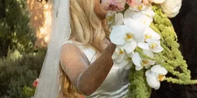 A bride in a white dress and veil holds a large, cascading bouquet of white orchids and greenery while embracing a groom.