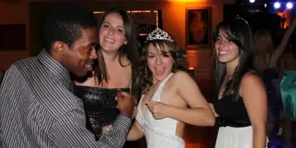 A group of young people, including a girl wearing a tiara, dancing and celebrating at a party.