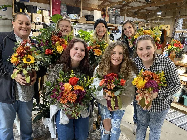 A group of people holding colorful floral arrangements in a workshop setting.