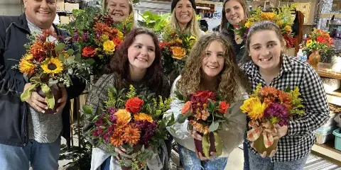A group of people holding colorful floral arrangements in a workshop setting.