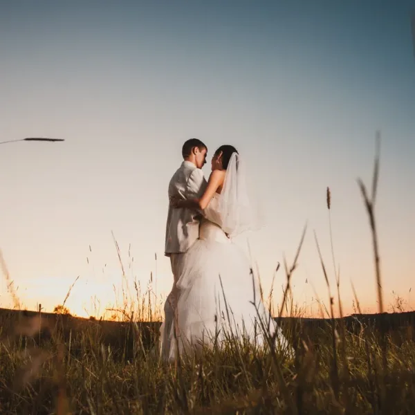 A bride and groom embracing in a field at sunset.