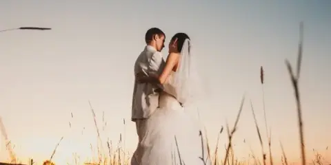 A bride and groom embracing in a field at sunset.