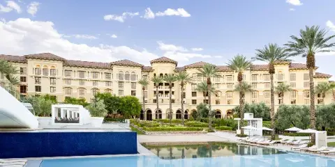 Exterior view of the Green Valley Ranch resort building with a swimming pool and palm trees in the foreground.