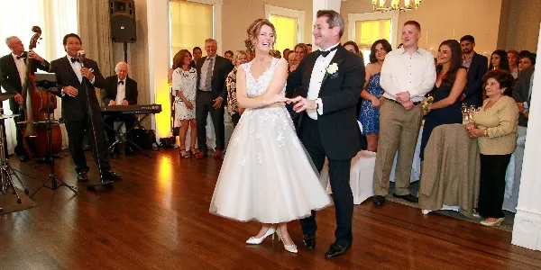 A bride and groom dancing at a wedding reception with guests and a live band in the background.
