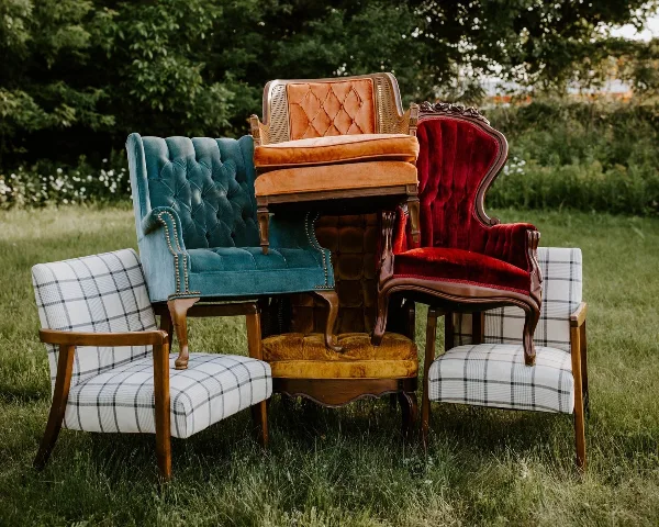 A group of vintage upholstered armchairs and a velvet chair arranged on a grassy lawn.